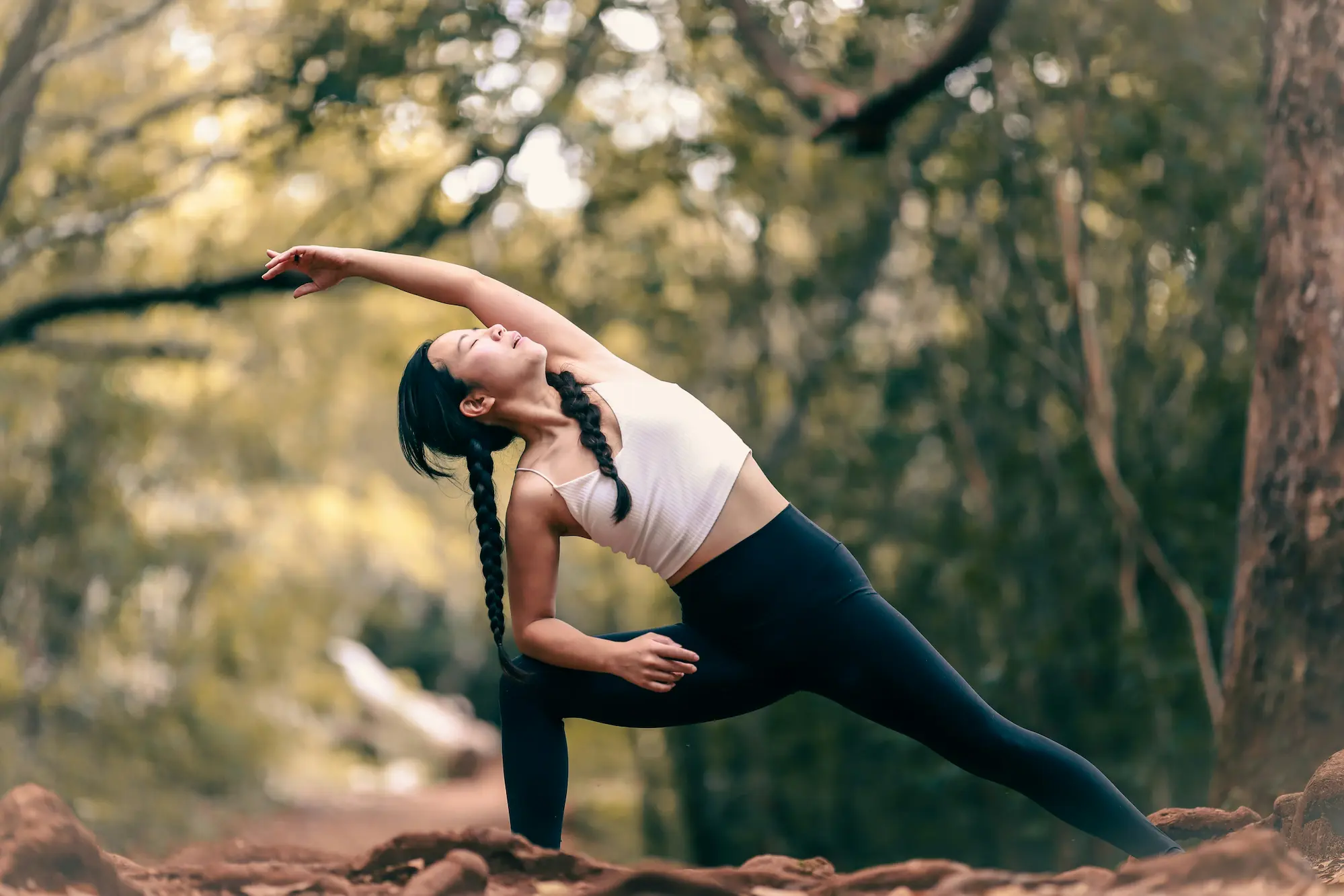 Woman practicing active stretching for fitness outdoors in a yoga side angle pose, surrounded by nature.